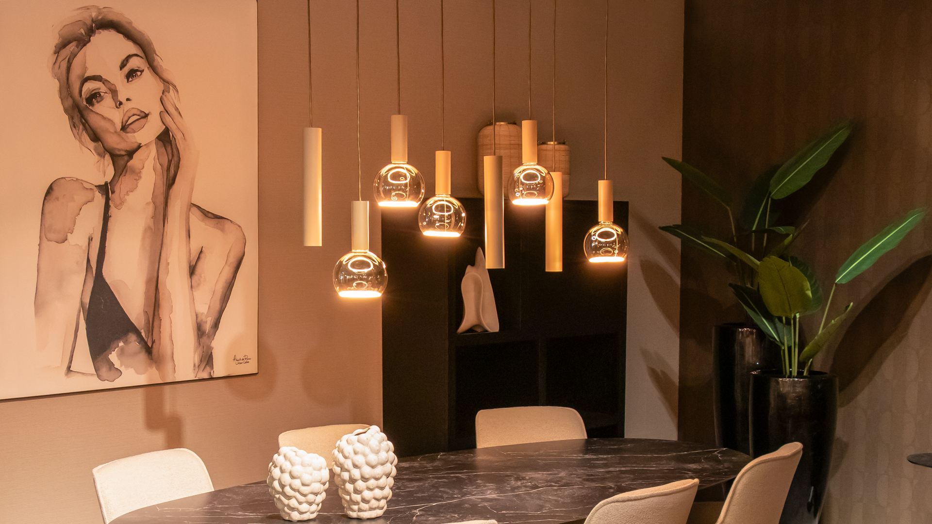 Sfeervolle eetkamer met warm verlichte hanglampen in cilindrische en bolvormige designs boven een donkere, ovale eettafel.