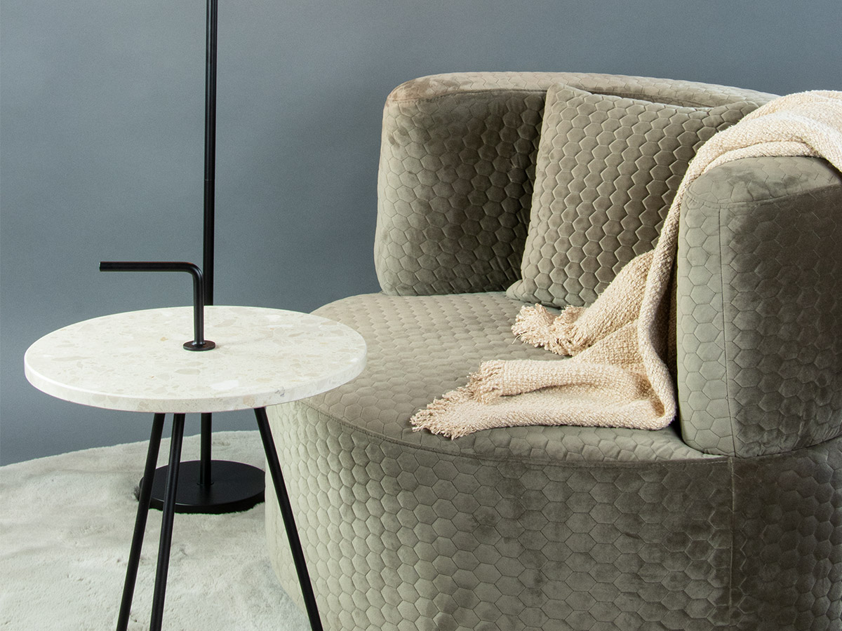 Groene velvet fauteuil met honingraatstructuur naast ronde terrazzo bijzettafel en zwarte vloerlamp