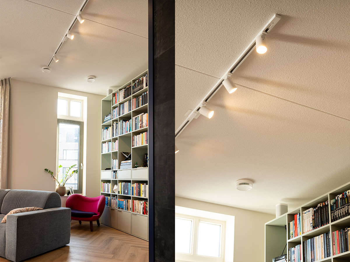 Witte railverlichting met richtbare spots boven een woonkamer en boekenkast, lichtoplossing ontworpen door Straluma.