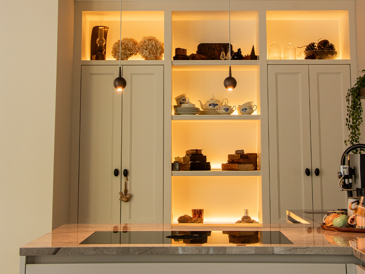 Minimalistische hanglampjes met warm licht boven kookeiland en verlichte vitrinekast in moderne keuken in Hendrik-Ido-Ambacht, geplaatst door Straluma.