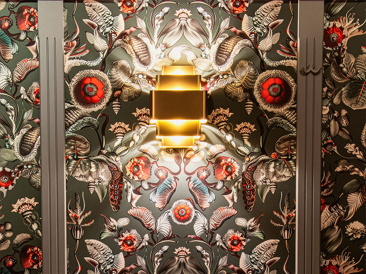 Gouden wandlamp van Straluma tegen een rijk gedecoreerde botanische muur bij Het Wapen van Rhoon.