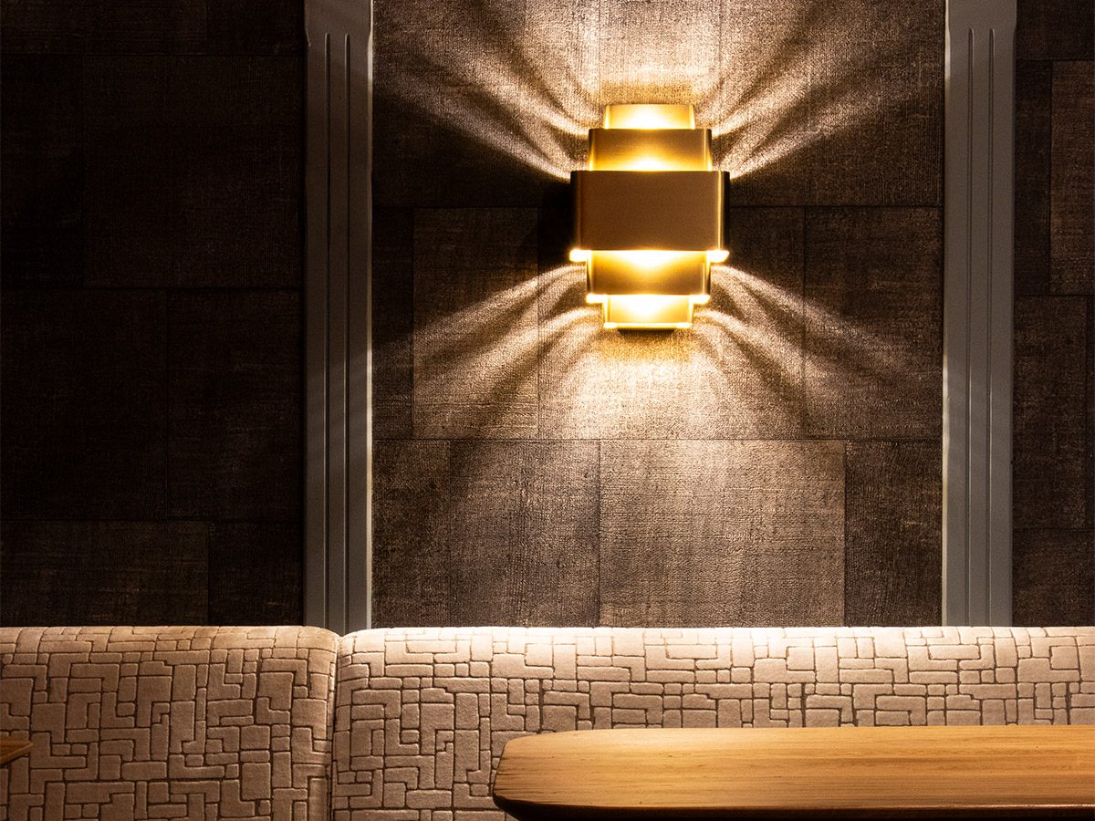 Gouden wandlamp van Straluma met prachtig lichtspel tegen een donkere wand bij Het Wapen van Rhoon.