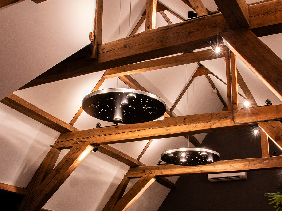 Moderne zwarte hanglampen van Straluma tussen karakteristieke houten balken bij Het Wapen van Rhoon.