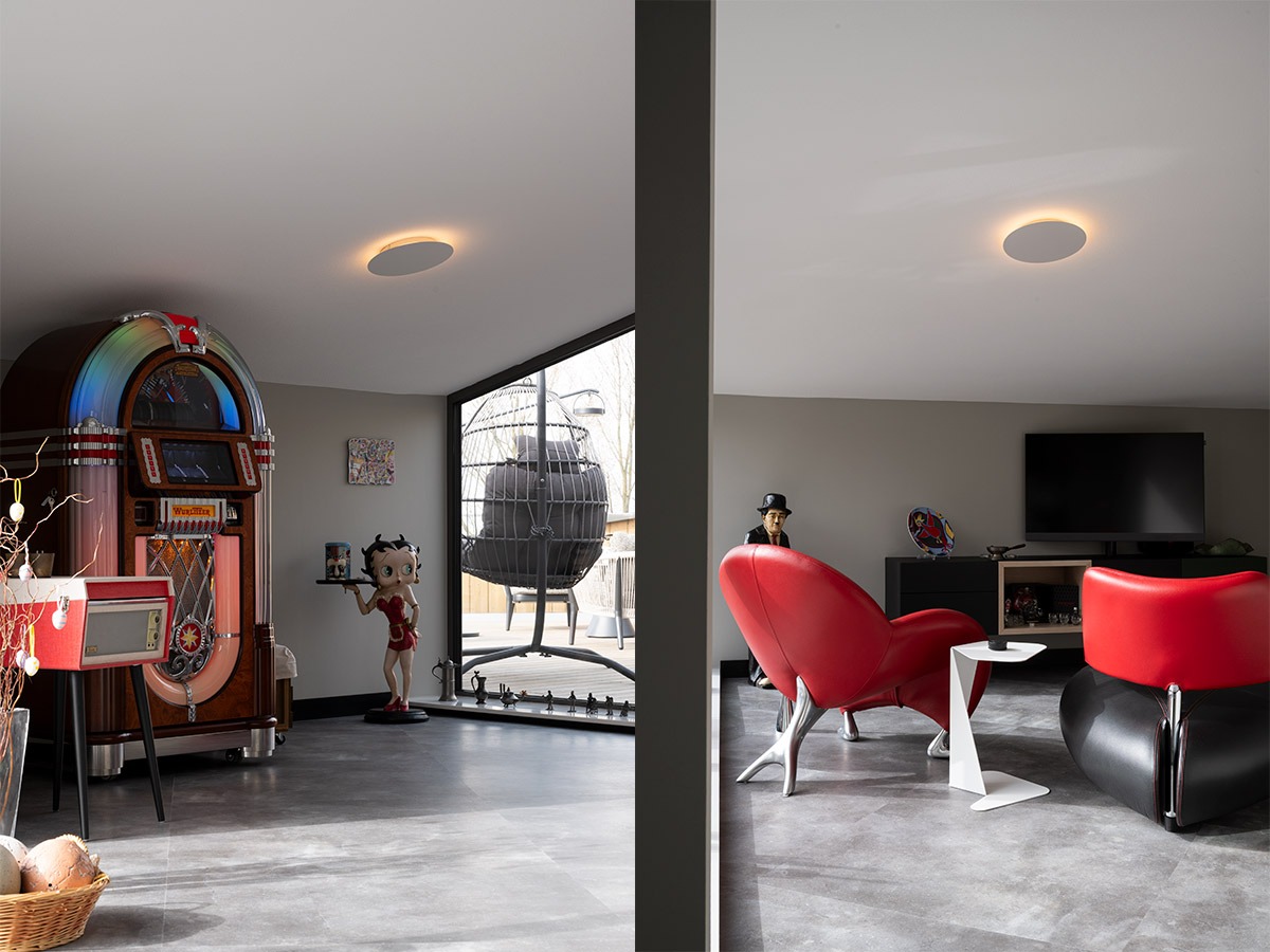 Woonkamer penthouse met plafondlamp, rode designstoelen en grote raampartij