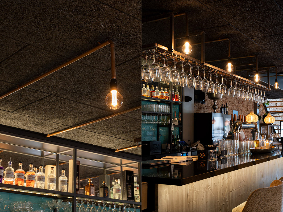 Industriële barverlichting met filamentlampen boven een moderne horecabar met flessenrek en wijnglazen