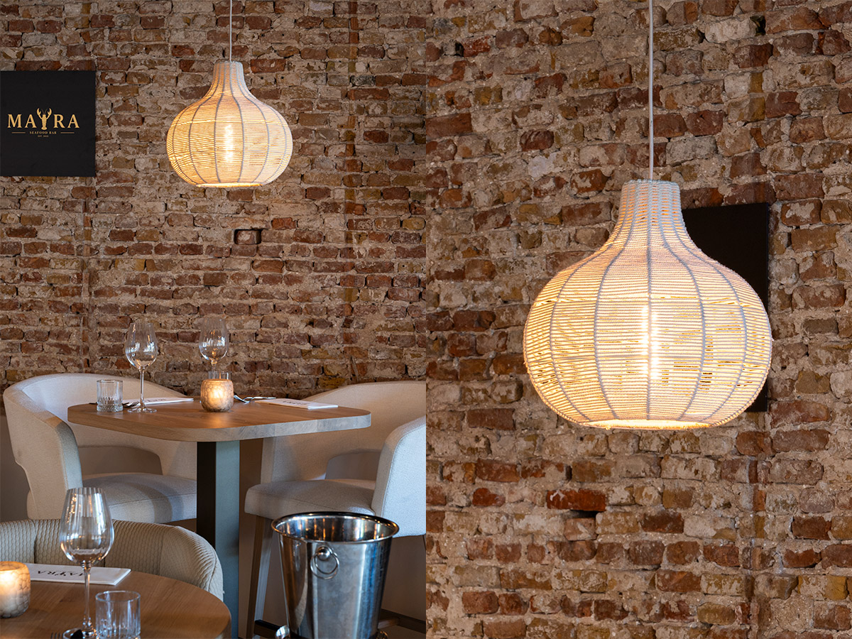 Hanglamp van rotan boven een restauranttafel tegen een karakteristieke bakstenen muur