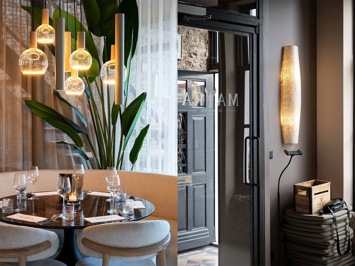 Sfeervol restaurantinterieur met design hanglampen boven een ronde tafel en decoratieve wandlamp naast de entree
